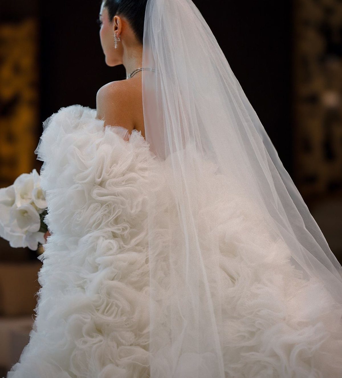 A bride in a white ruffled wedding dress with a long sheer veil.
