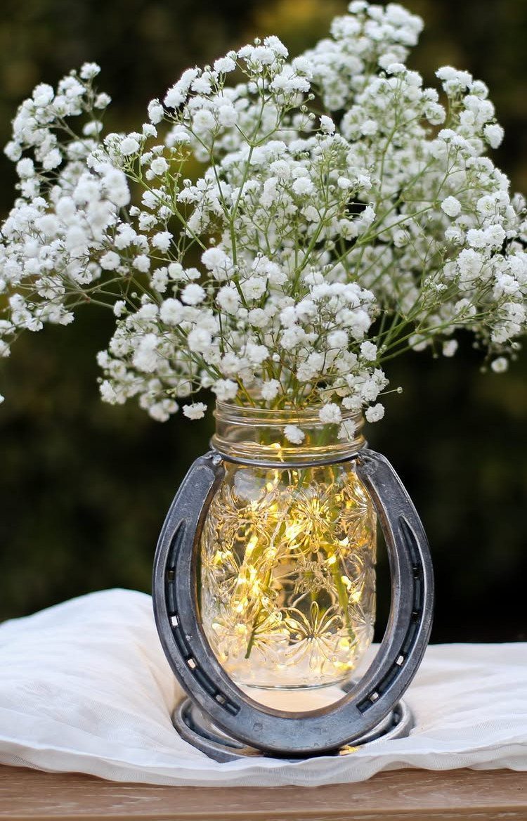 A mason jar filled with fairy lights and baby's breath inside a horseshoe frame.