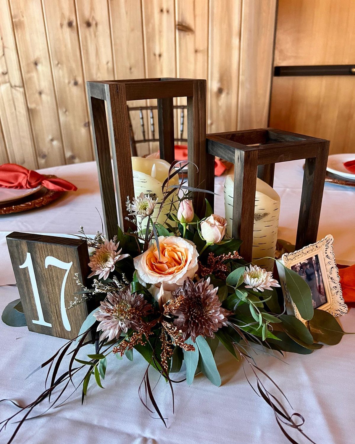 Rustic centerpiece with wooden lanterns, peach roses, greenery, and a wooden table number seventeen.