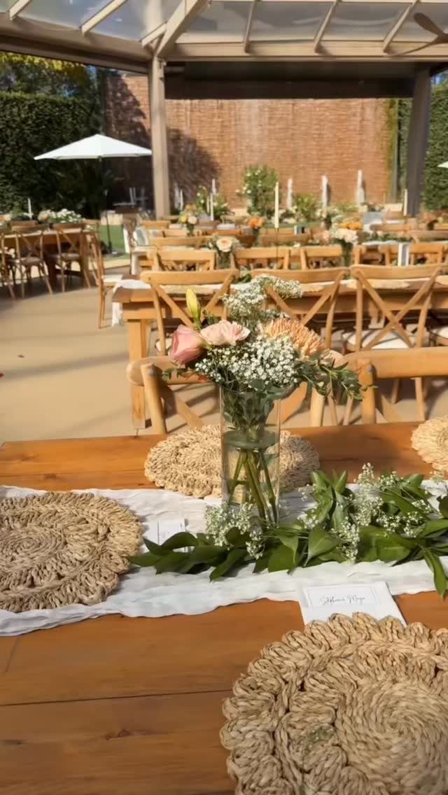 Wooden wedding table set with white runner, floral arrangements, greenery, and woven straw placemats.