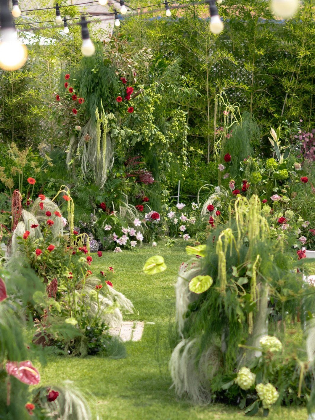 Floral arrangements with red and pink flowers and green foliage under hanging string lights.