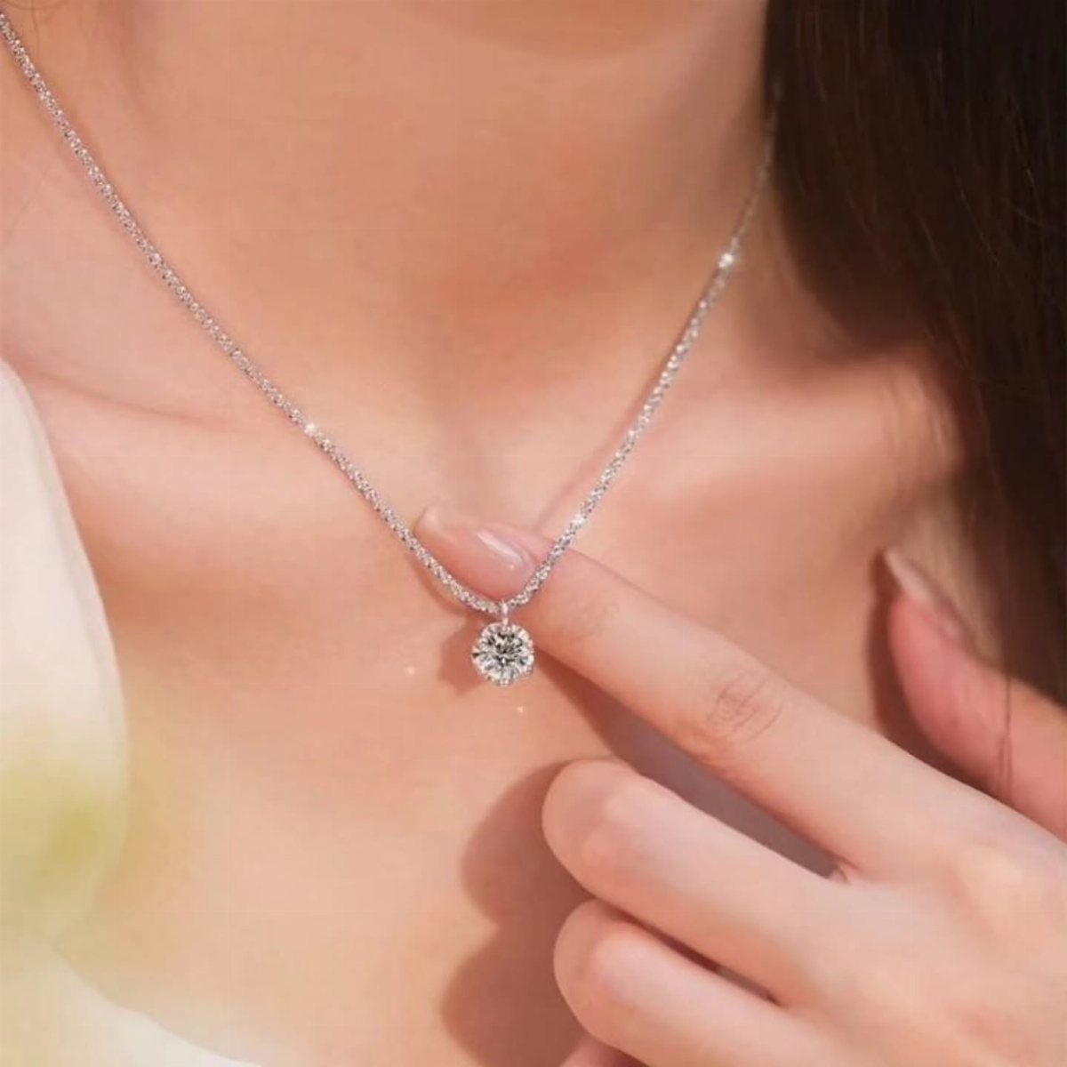 5 Silver Necklace Wedding Looks for Every Bridal Style 1 A delicate silver chain necklace featuring a single sparkling round gemstone pendant on a person's neck.