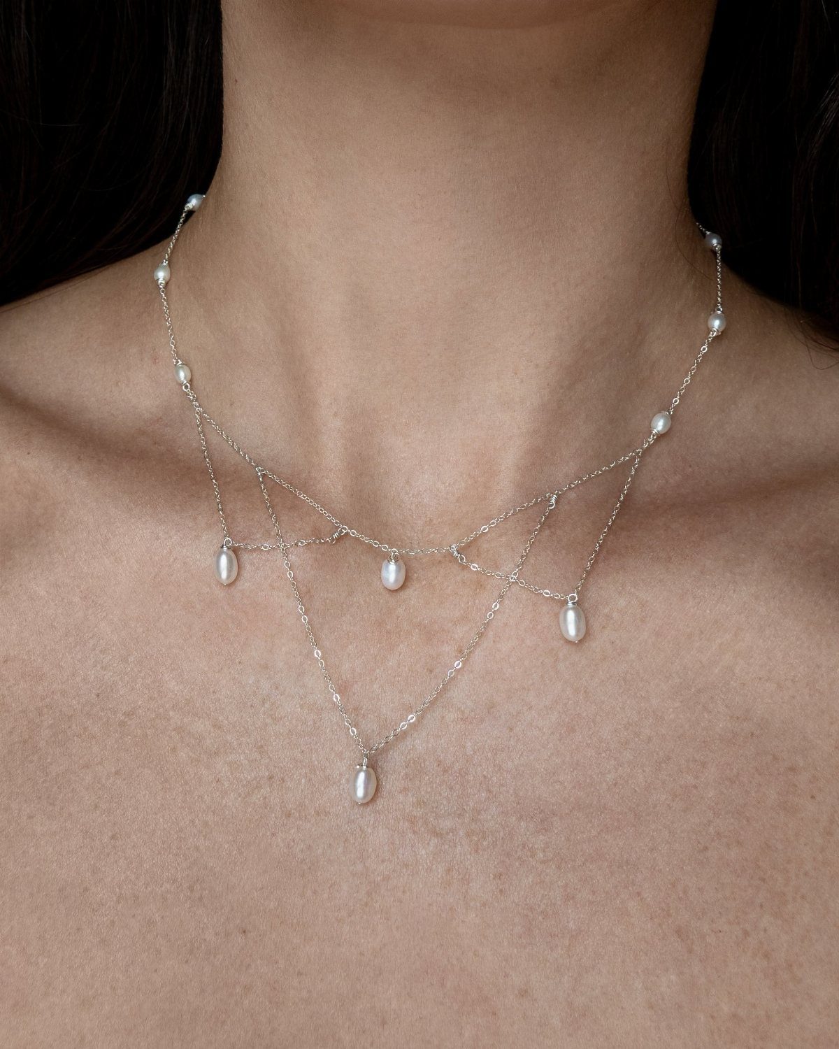 5 Silver Necklace Wedding Looks for Every Bridal Style 2 A person wearing a layered silver necklace with delicate chains and hanging white pearls.