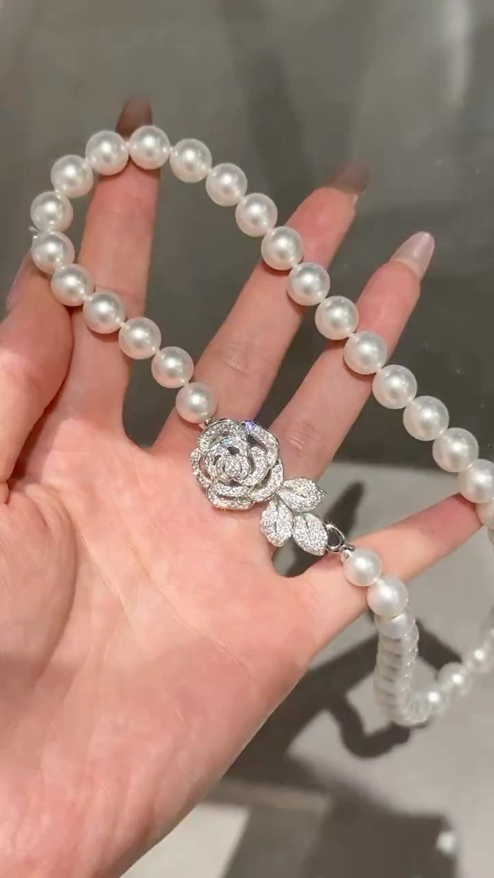 5 Silver Necklace Wedding Looks for Every Bridal Style 3 A hand holding a white pearl necklace with a silver rose-shaped crystal centerpiece.