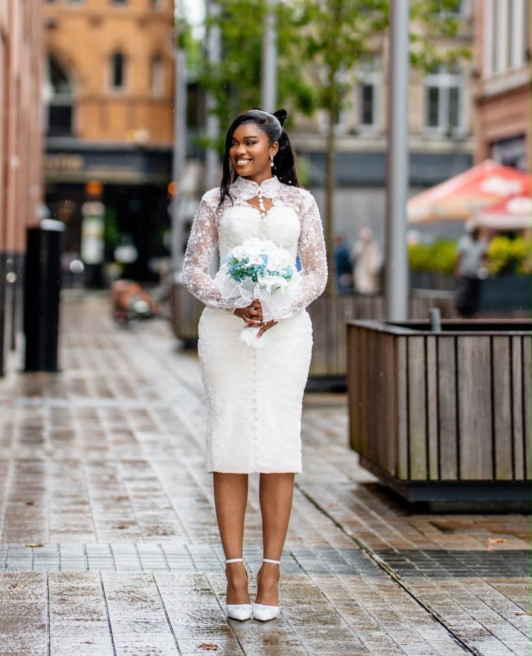 Simple Court Wedding Dress: 7 Styles That Work at City Hall 5 A woman in a white lace sheath dress holding a bouquet on a city street.