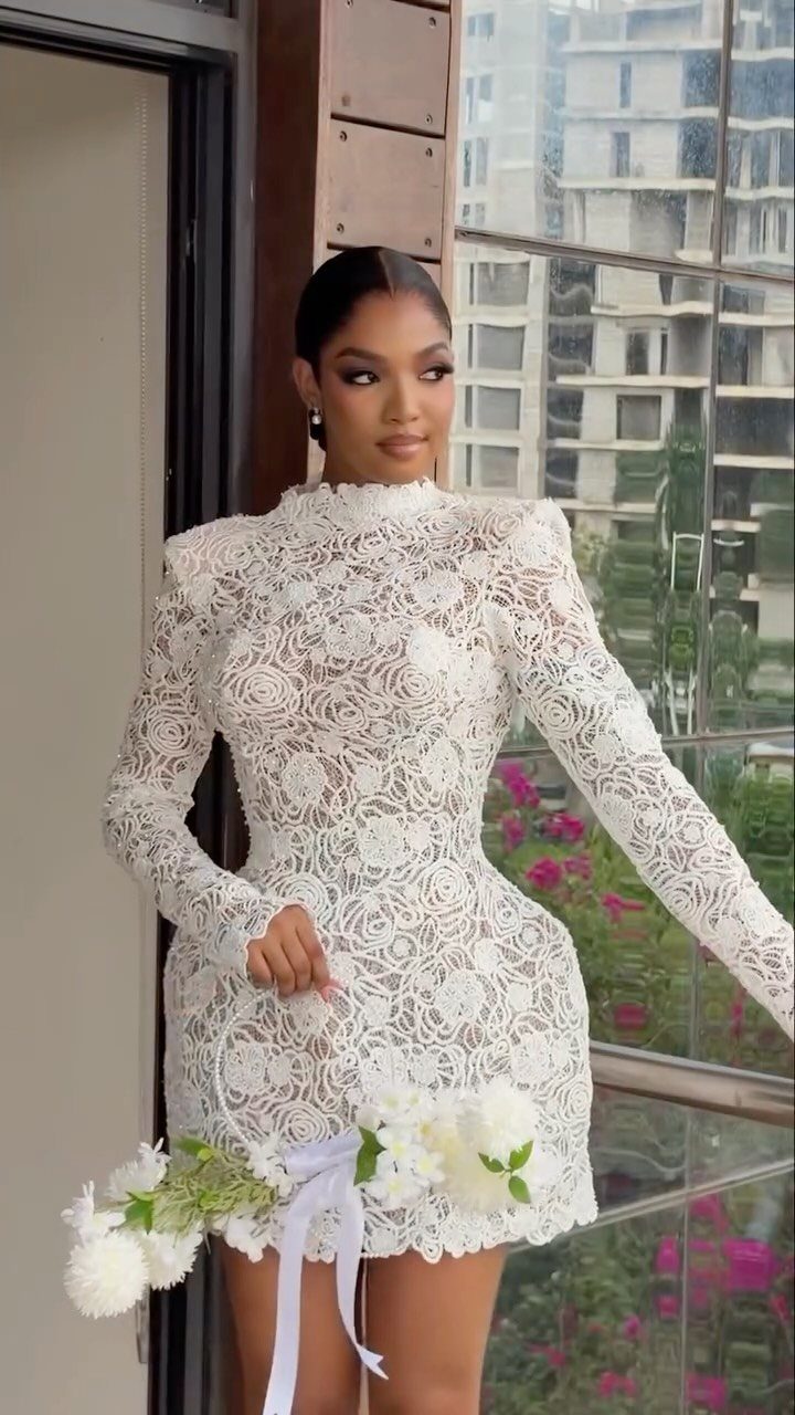 Simple Court Wedding Dress: 7 Styles That Work at City Hall 4 A woman in a long-sleeved white lace mini dress holding a white flower bouquet.
