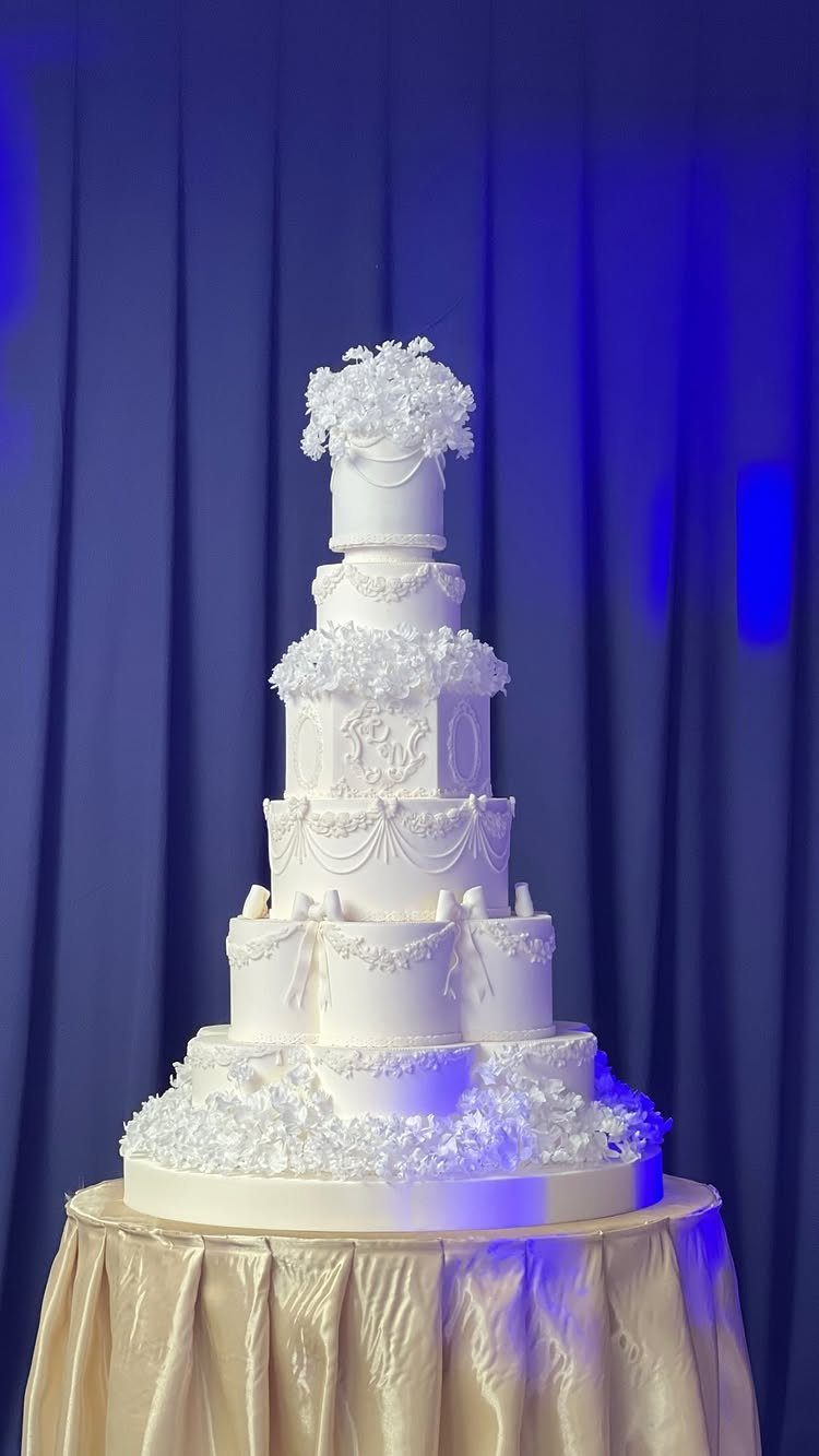 13 Wedding Cakes with Flowers to Suit Every Style 10 A tall white multi-tiered wedding cake decorated with white flowers and intricate frosting patterns.