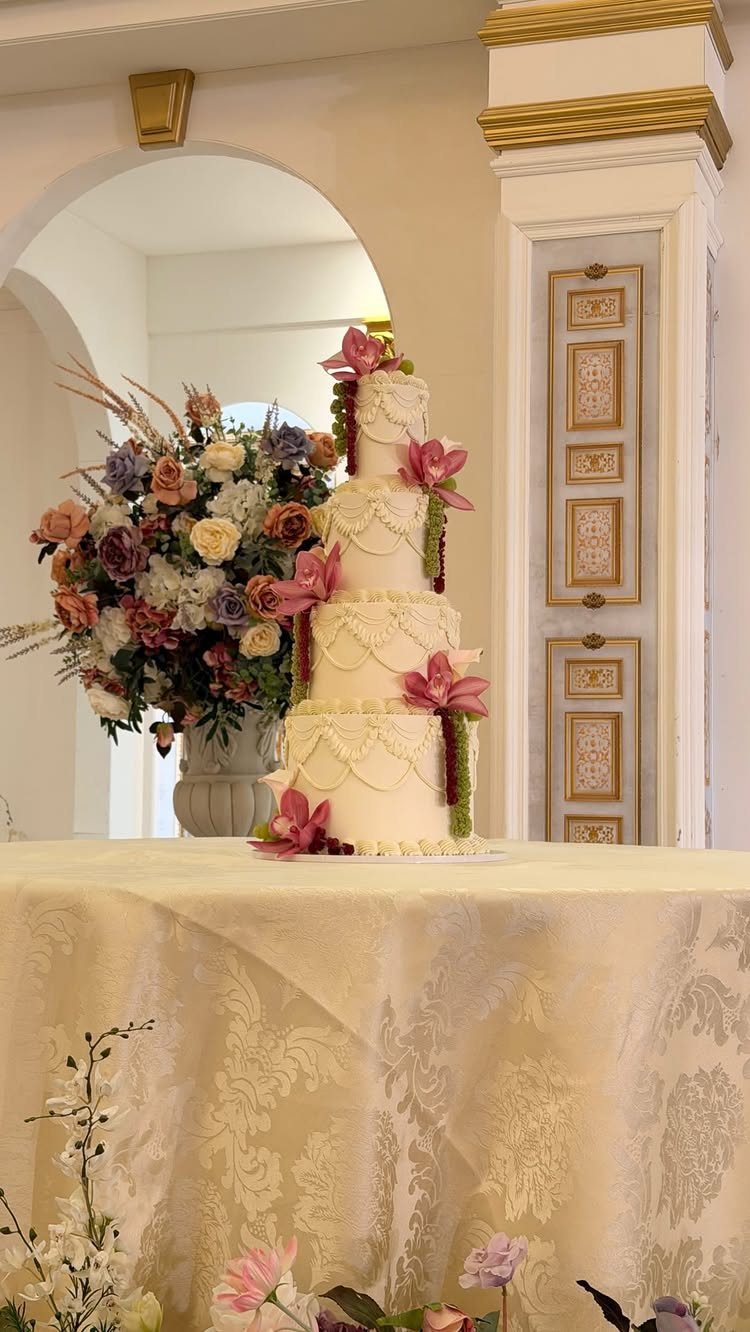 13 Wedding Cakes with Flowers to Suit Every Style 5 A white tiered wedding cake decorated with pink lilies and pearl frosting on a tablecloth.