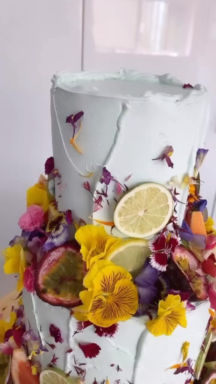 13 Wedding Cakes with Flowers to Suit Every Style 4 A two-tier light blue cake decorated with colorful pansies, lemon slices, and passion fruit.