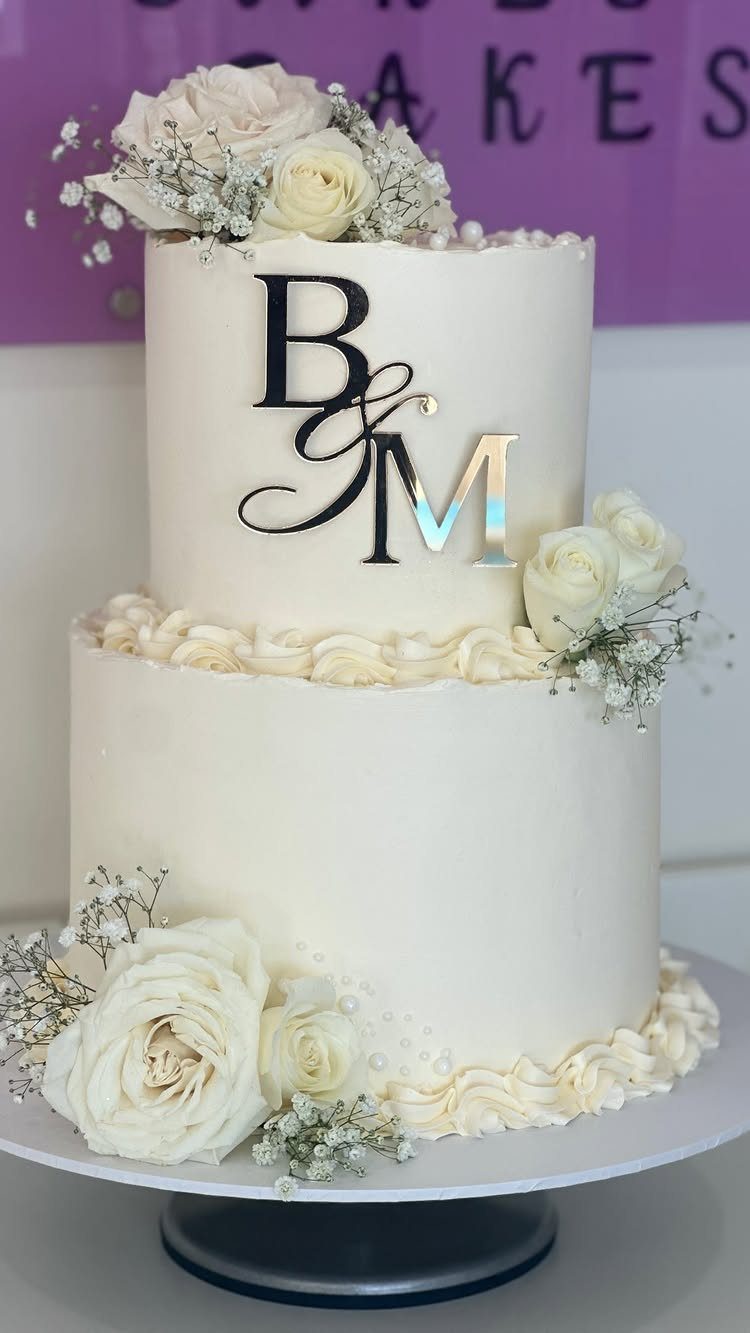 13 Wedding Cakes with Flowers to Suit Every Style 11 Two-tier white wedding cake decorated with white roses, baby's breath, and silver initials.