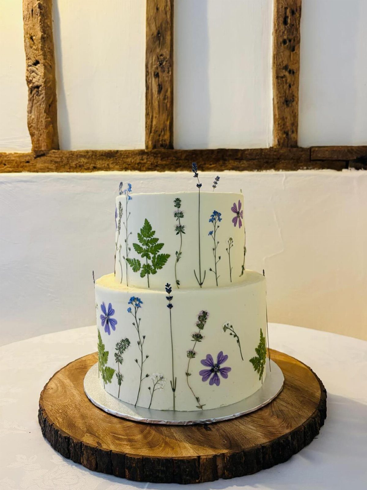13 Wedding Cakes with Flowers to Suit Every Style 12 A two-tier white wedding cake decorated with various small purple and blue edible flowers and green leaves.