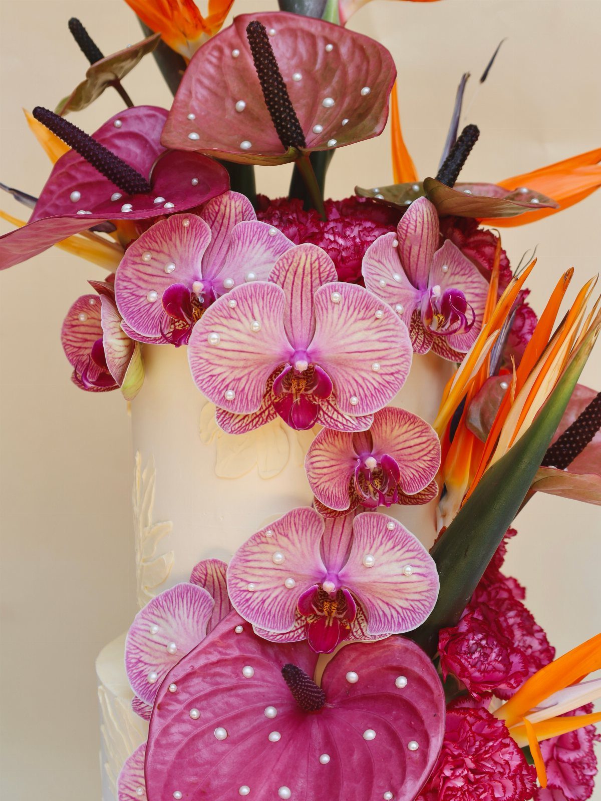 13 Wedding Cakes with Flowers to Suit Every Style 7 A white wedding cake decorated with pink orchids, anthuriums, and orange bird of paradise flowers.