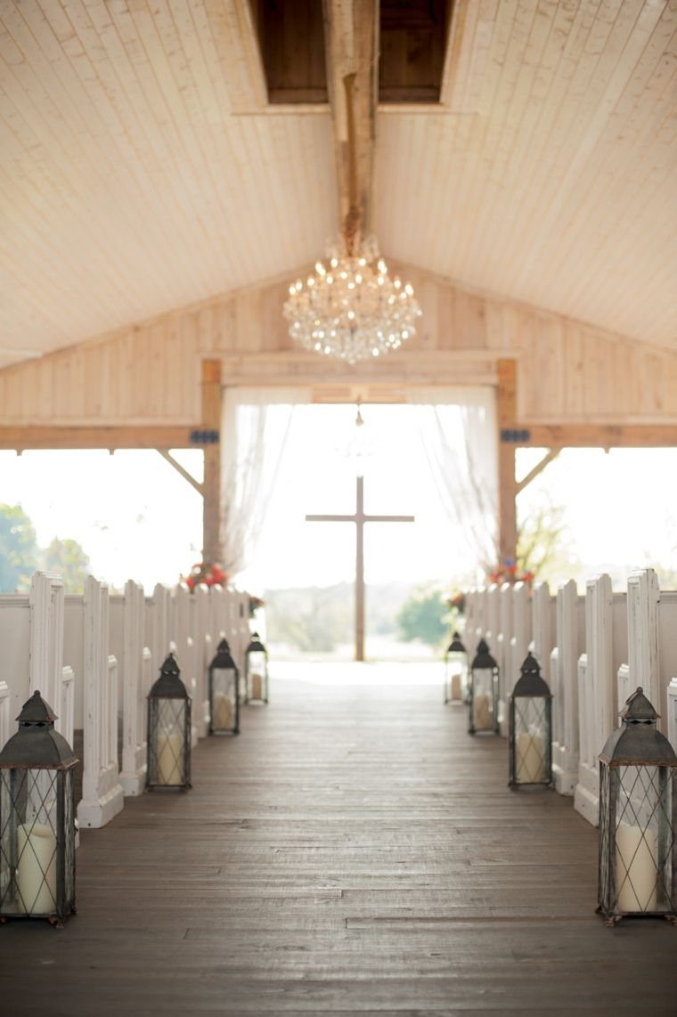 Black lanterns with white candles line a wooden aisle leading toward a wooden cross.