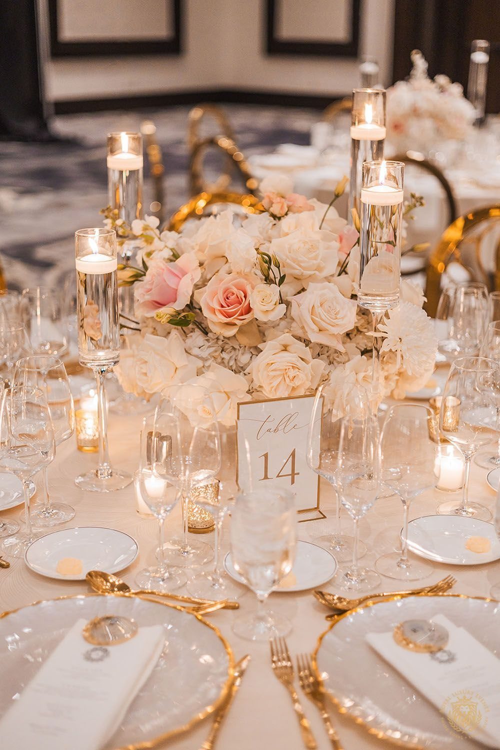 Blush and cream rose centerpiece on a wedding table with gold cutlery and candles.