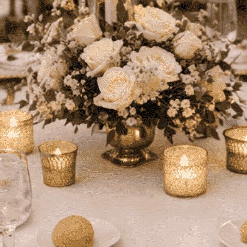 Elegant wedding table setting with gold cutlery, champagne napkins, and white rose floral arrangements.