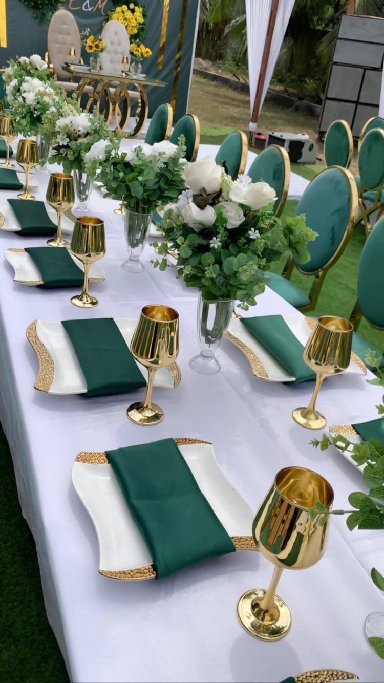 A wedding table set with emerald green napkins, gold-rimmed plates, and white floral centerpieces.
