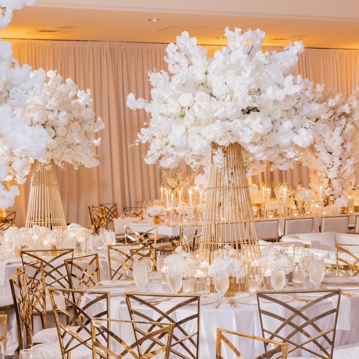 Large white floral arrangements on tall gold metallic stands at a wedding reception table.