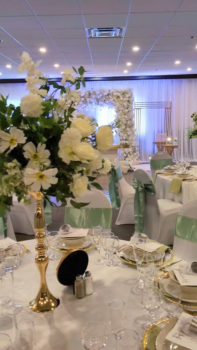 Wedding table setting with white linens, gold chargers, and sage green chair sashes.
