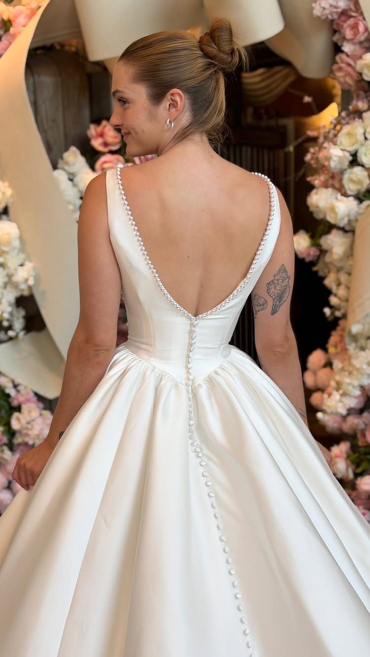 Wedding Dress Backs: 10 Styles That Turn the Exit Into a Moment 8 Woman in a white satin wedding dress featuring a deep V-back and a row of buttons.