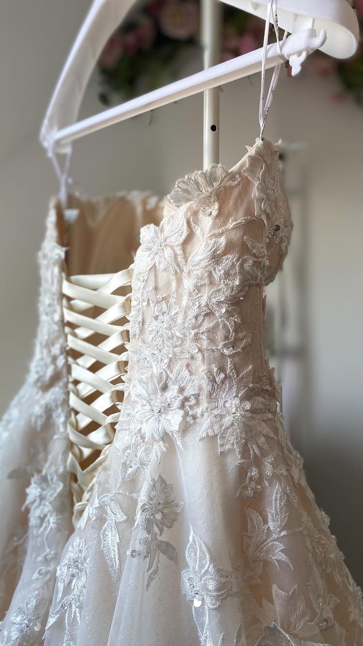 Wedding Dress Backs: 10 Styles That Turn the Exit Into a Moment 3 A cream lace wedding dress with a corset back hanging on a white hanger.