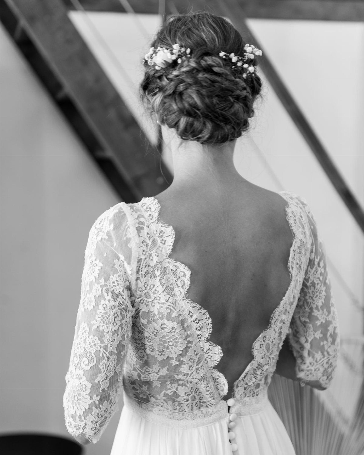 Wedding Dress Backs: 10 Styles That Turn the Exit Into a Moment 1 Woman in a lace wedding dress featuring a deep V-shaped back and floral hair accessory.