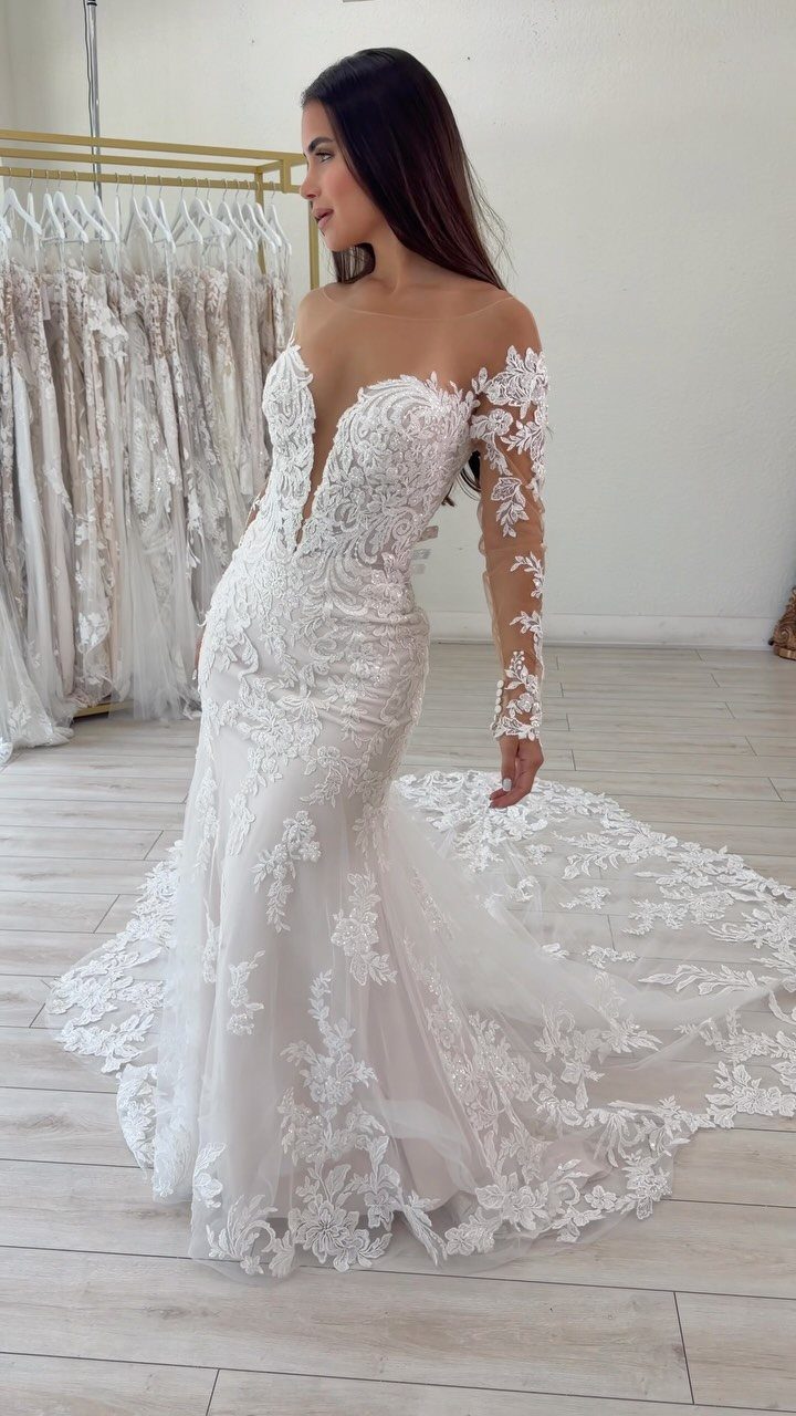Wedding Dress Backs: 10 Styles That Turn the Exit Into a Moment 10 Woman wearing a white lace wedding dress with a long, flowing lace train on a wooden floor.