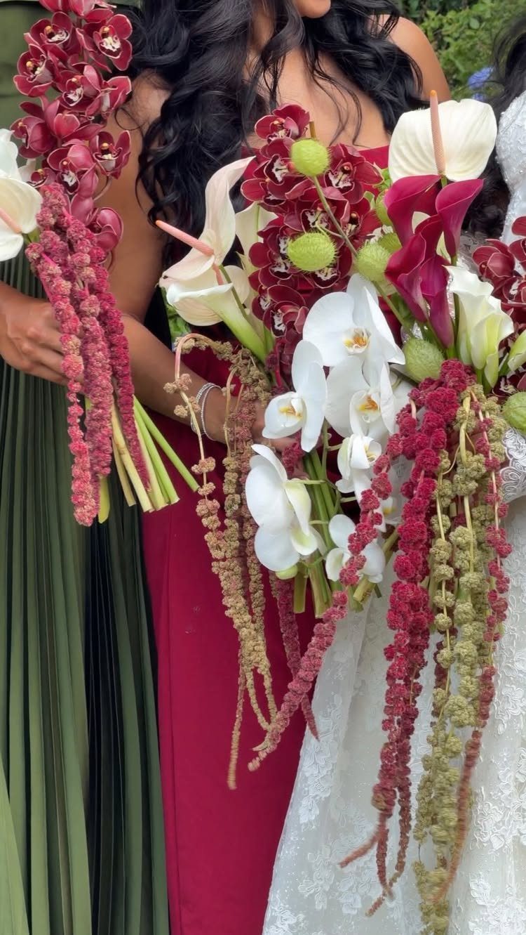 Women holding large bouquets of red and white flowers against green and red dresses.