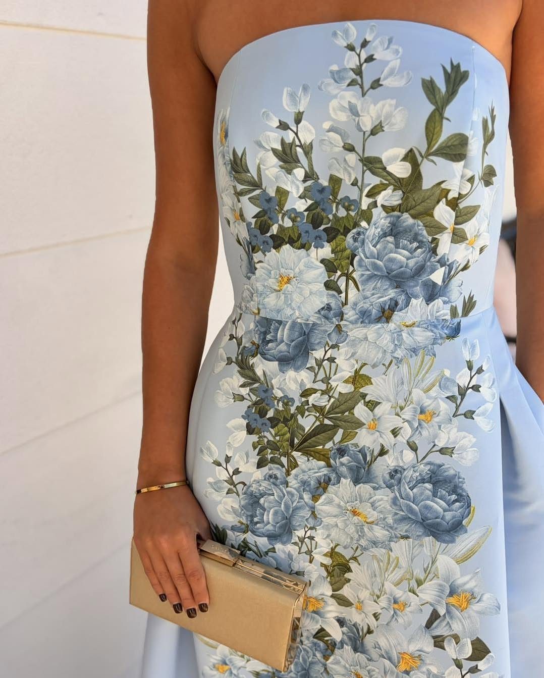 A person in a strapless light blue floral print dress holding a gold clutch.
