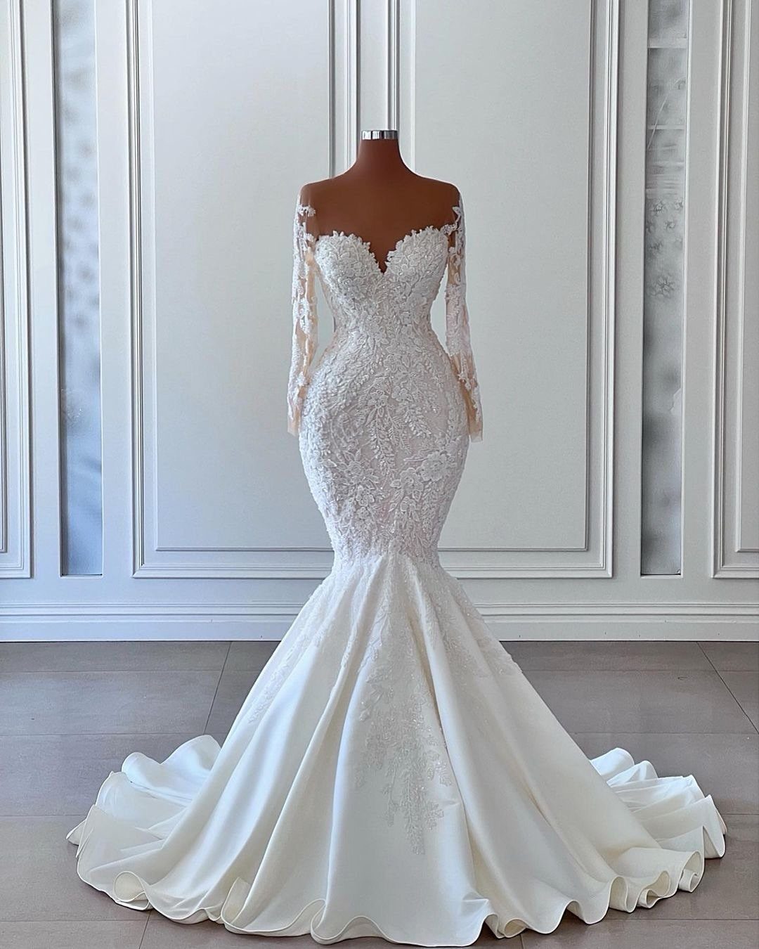 An ivory lace mermaid wedding dress displayed on a mannequin against a white wall.