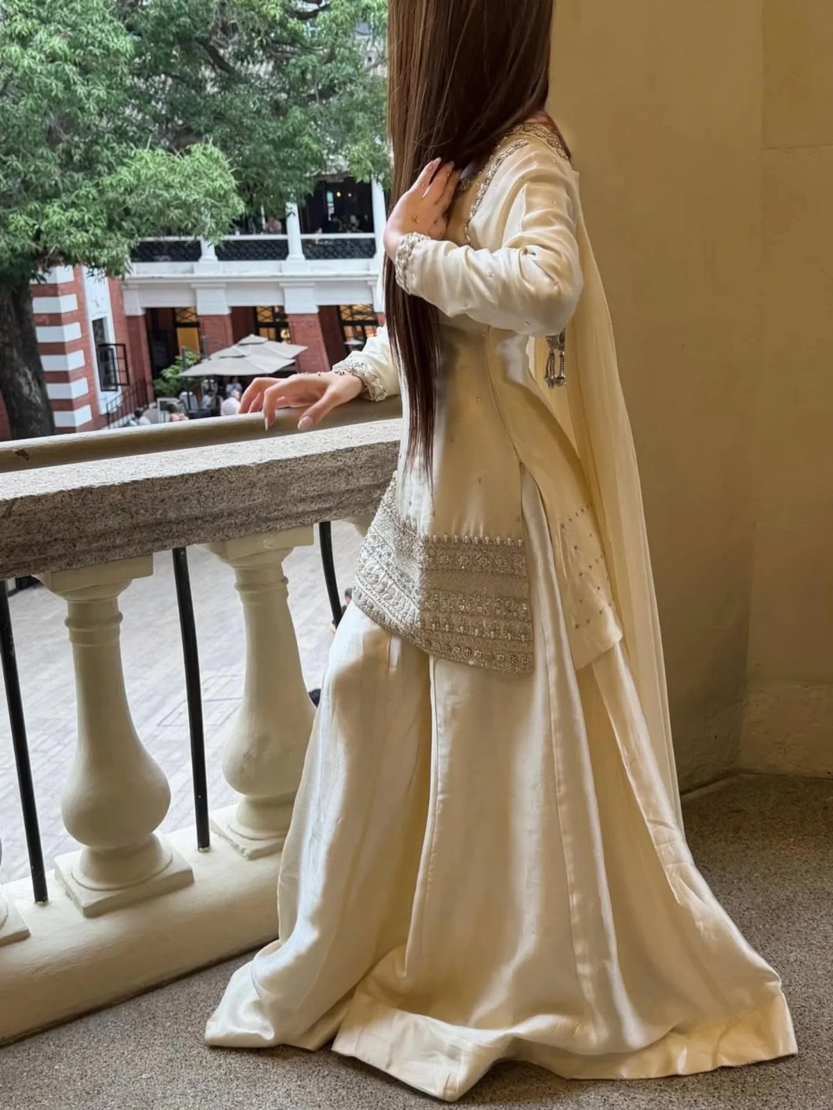 Woman in a cream embroidered traditional wedding outfit standing on a stone balcony overlooking trees.