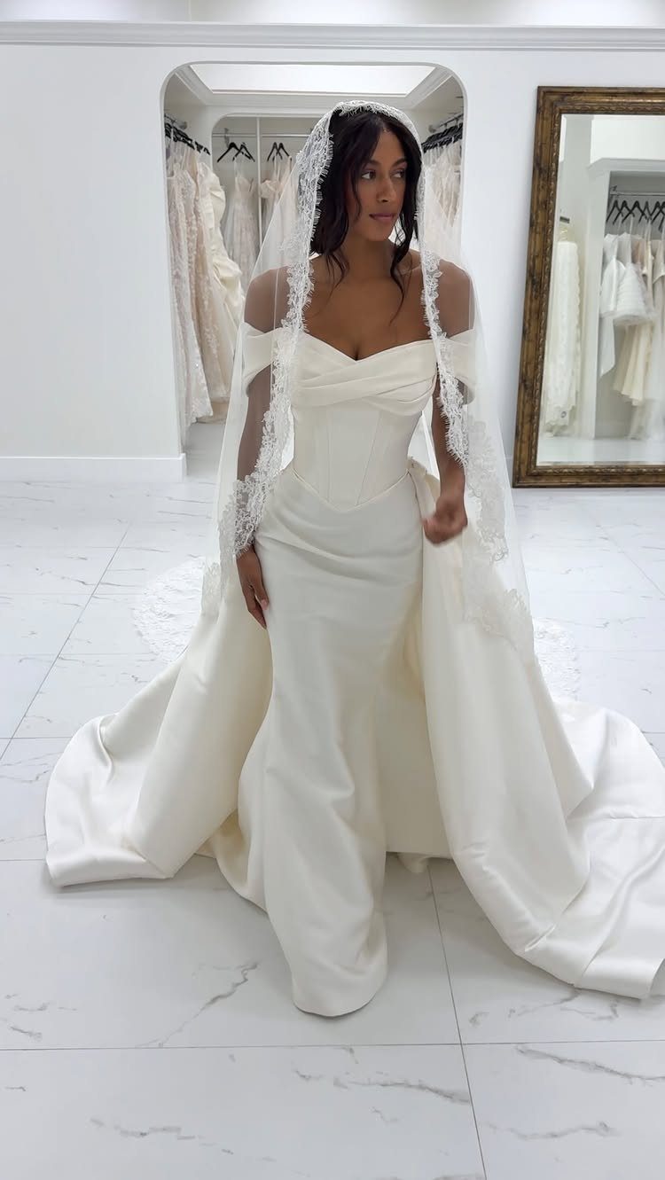 Woman wearing a white wedding dress and a long lace-edged veil in a boutique.