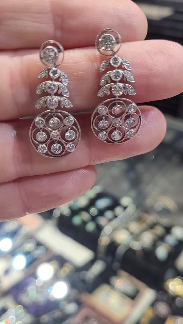A person holding a pair of silver diamond drop earrings against a blurred jewelry store background.