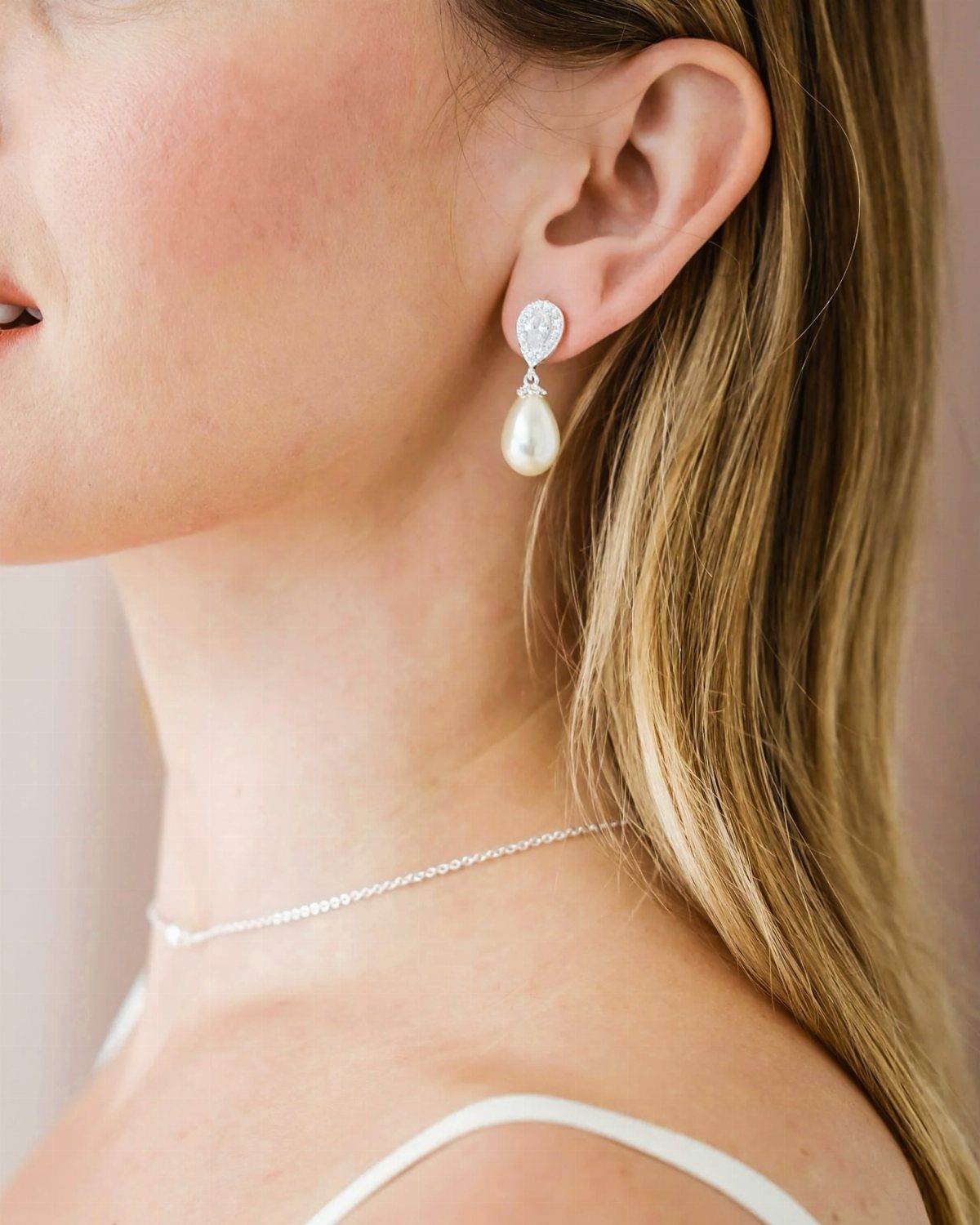 A woman wearing silver earrings with an oval crystal and a hanging teardrop pearl.