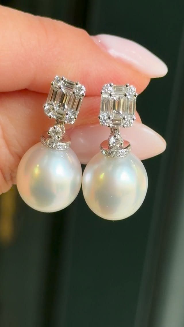 A hand holding large white pearl drop earrings with diamond accents.