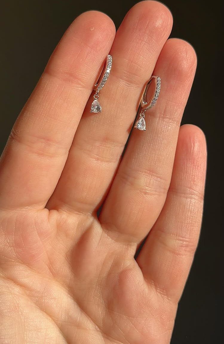 Two silver rhinestone drop earrings with teardrop pendants resting on an open human palm.