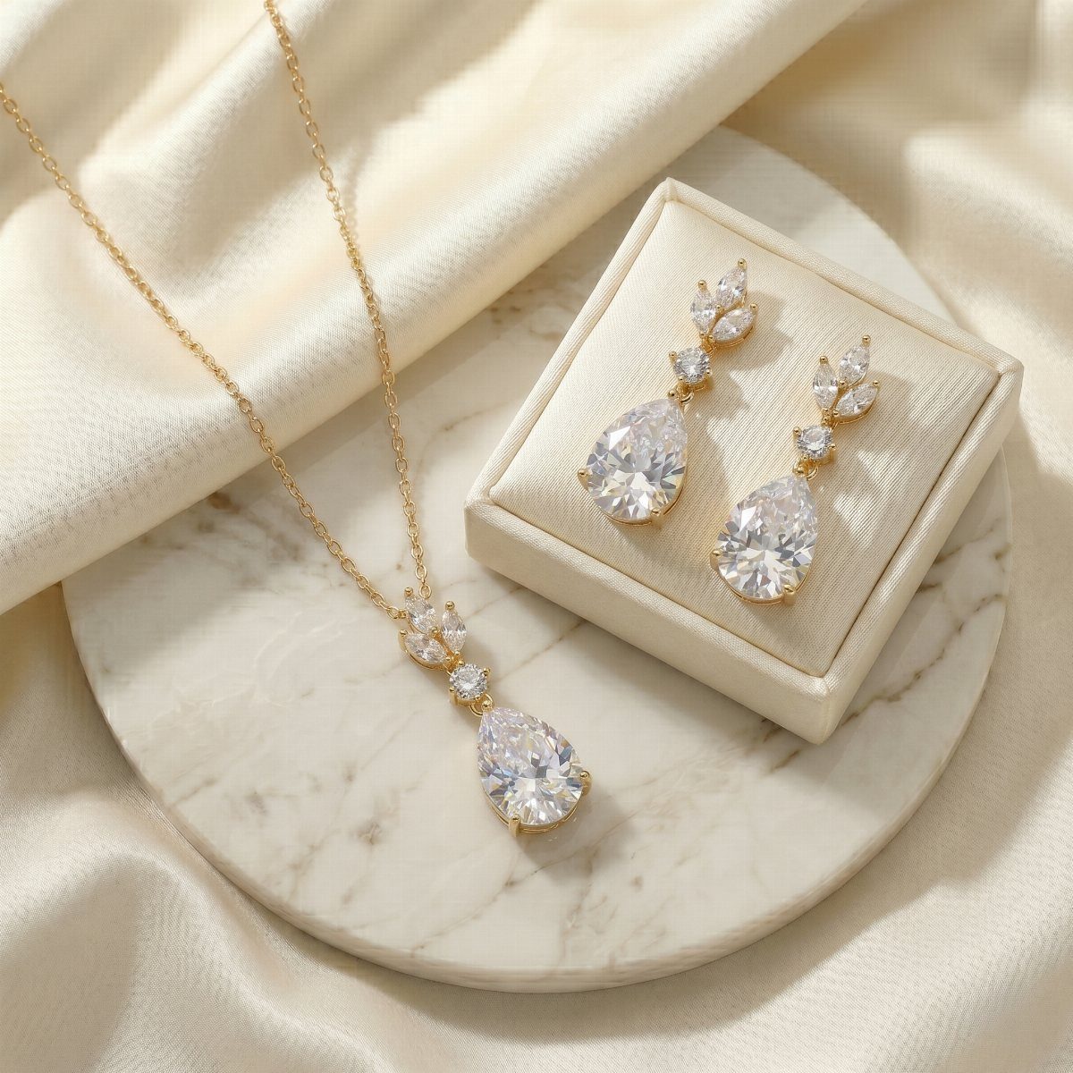 Gold-toned teardrop crystal pendant necklace and matching drop earrings on marble and jewelry box.