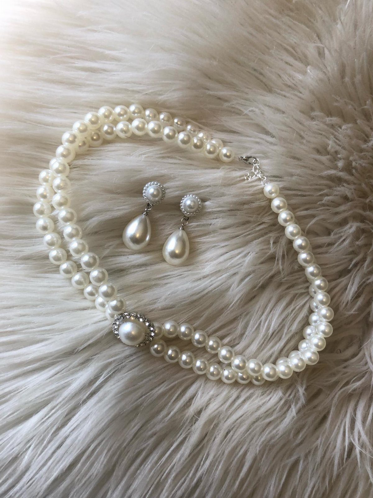 A two-strand pearl necklace with a crystal center and matching drop earrings on white fur.