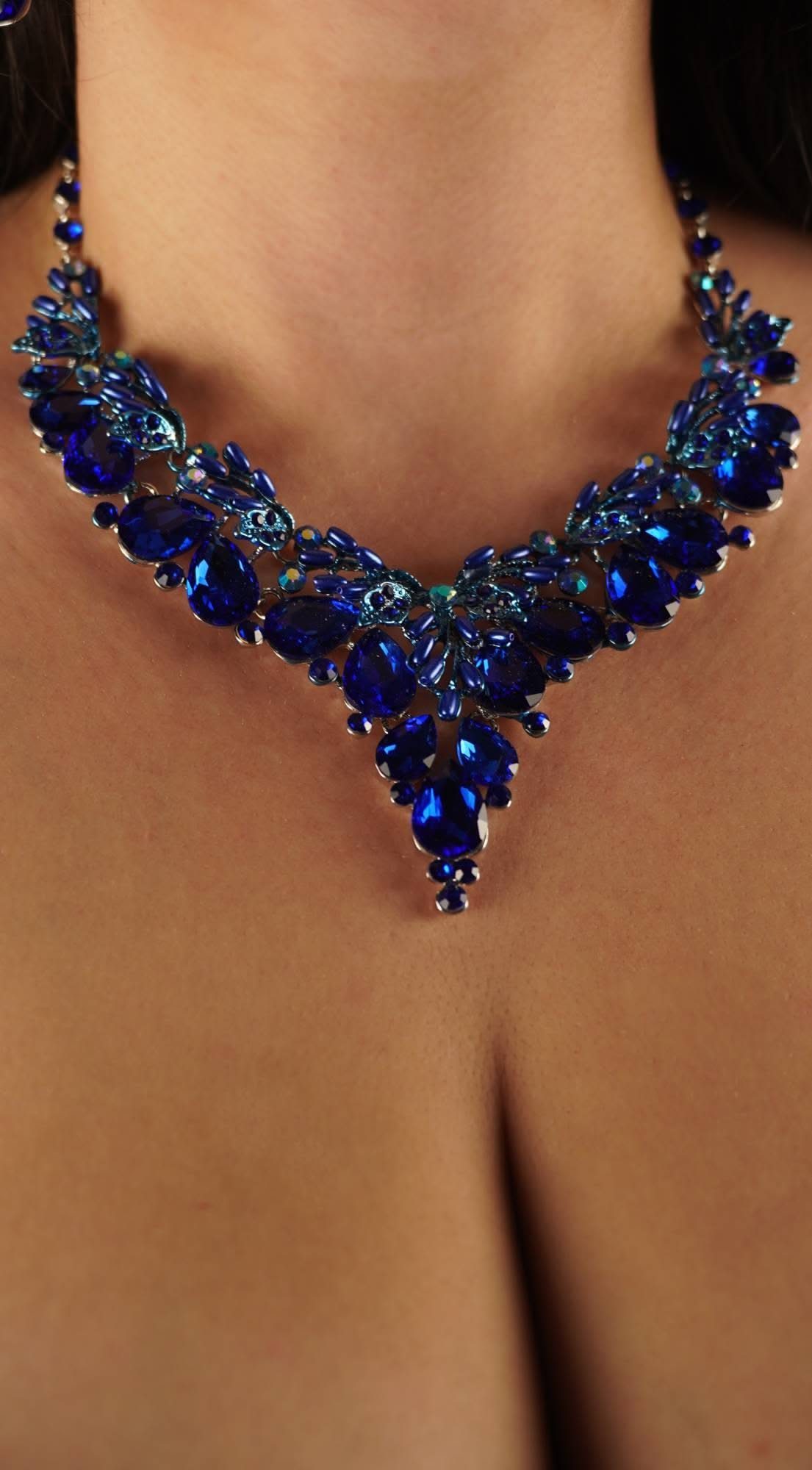 A person wearing a large, ornate navy blue crystal necklace with intricate silver-toned metalwork.