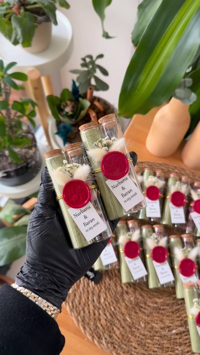 10 Wedding Favors for Guests Ideas: From Plants to Hot Sauce 10 A hand holding two personalized glass tubes filled with green stalks and dried flowers.