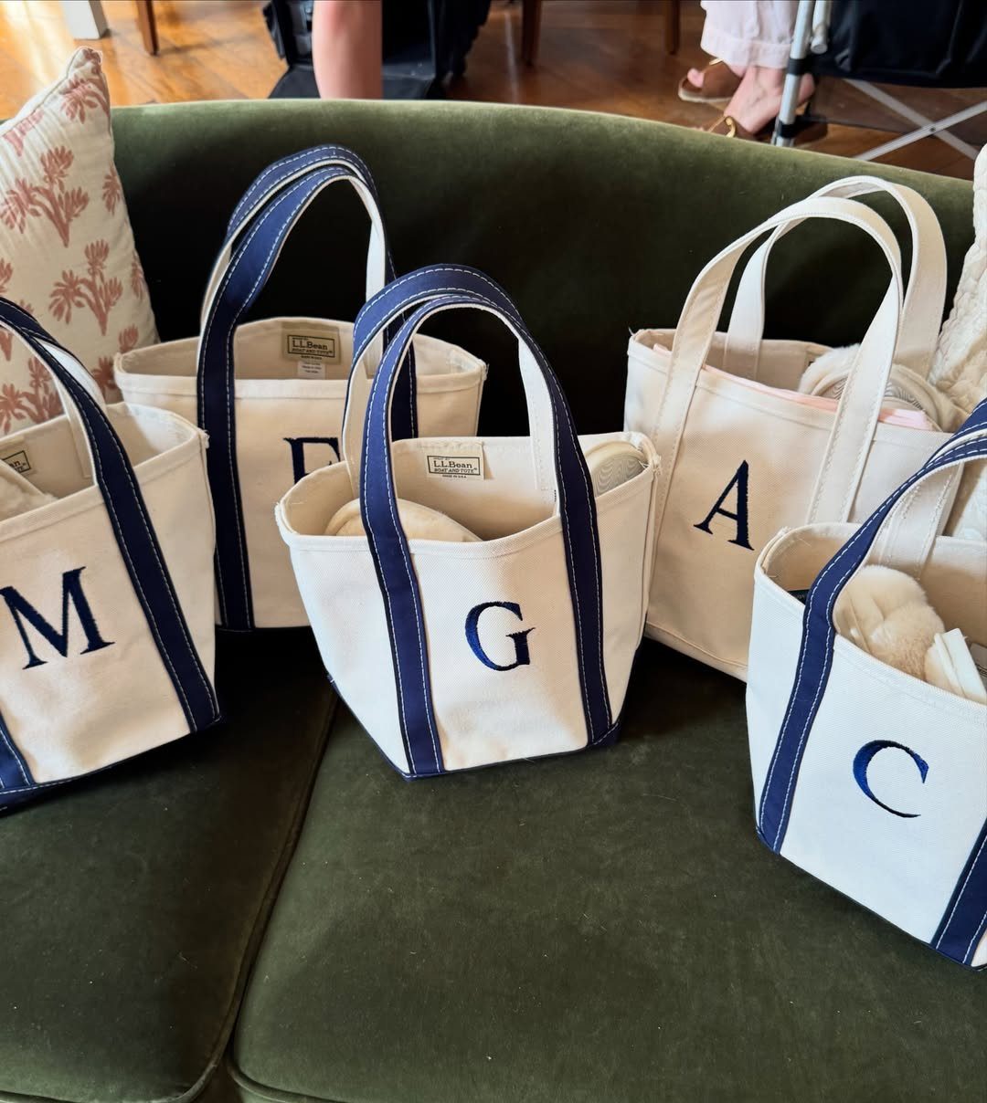 10 Wedding Favors for Guests Ideas: From Plants to Hot Sauce 6 Small monogrammed white canvas tote bags with blue handles resting on a green velvet sofa.