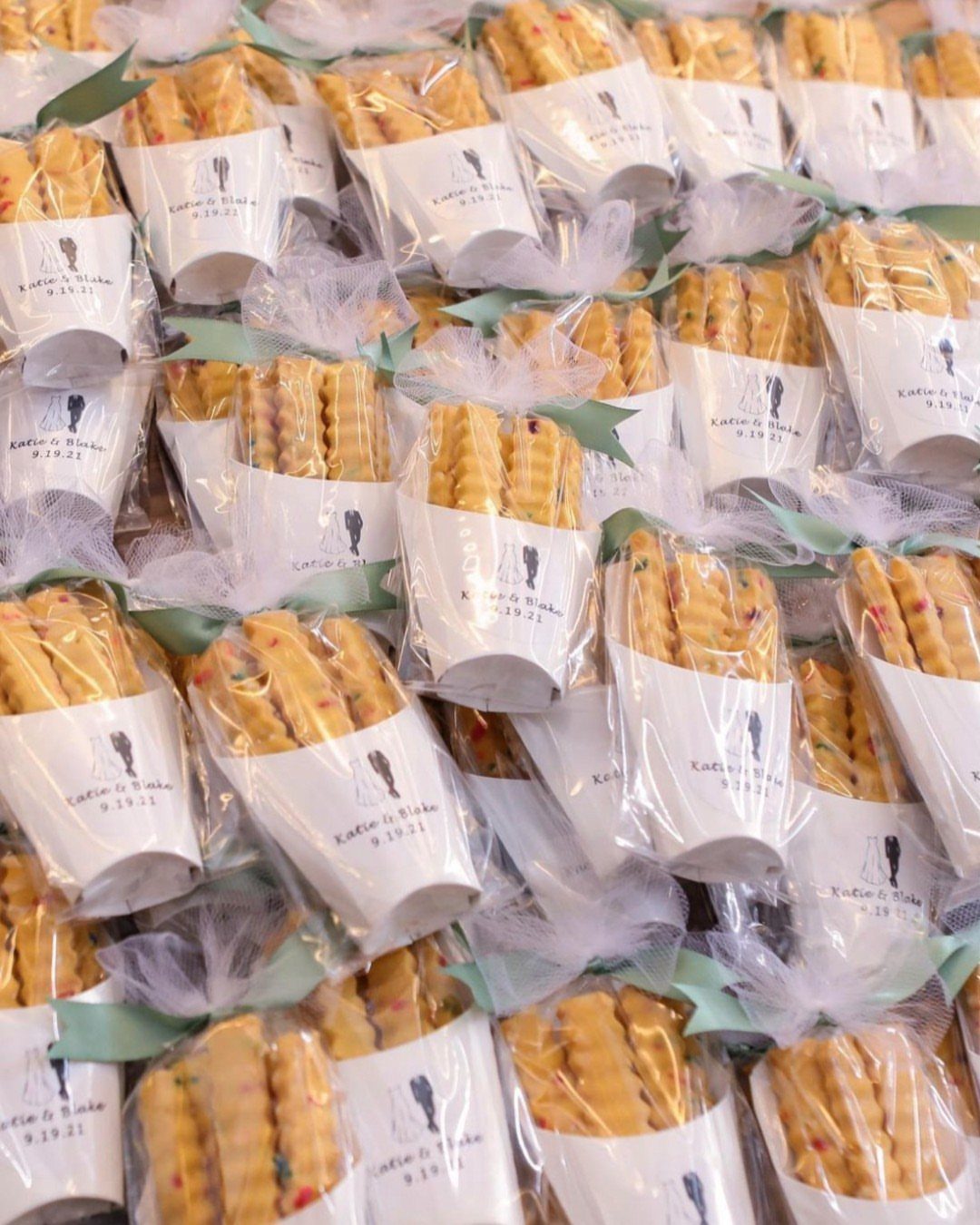 10 Wedding Favors for Guests Ideas: From Plants to Hot Sauce 1 Many small clear bags filled with golden cookies tied with white tulle ribbons.