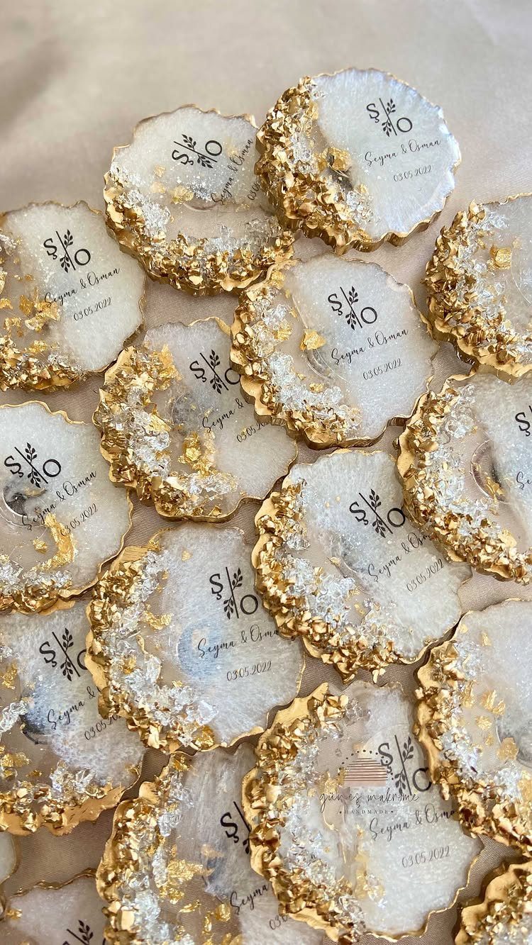 10 Wedding Favors for Guests Ideas: From Plants to Hot Sauce 4 Numerous white agate coasters with gold edges and personalized black text scattered on a surface.