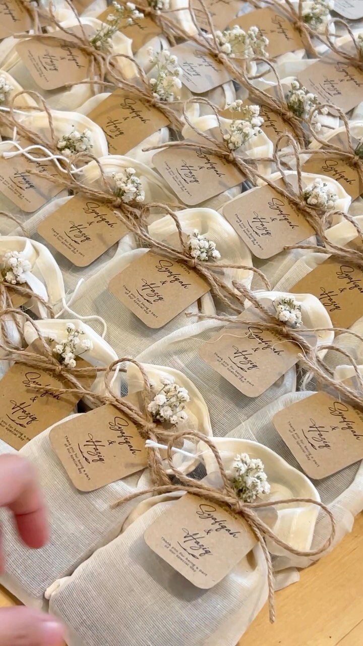 Small cream fabric pouches with twine, dried flowers, and personalized kraft paper tags arranged in rows.