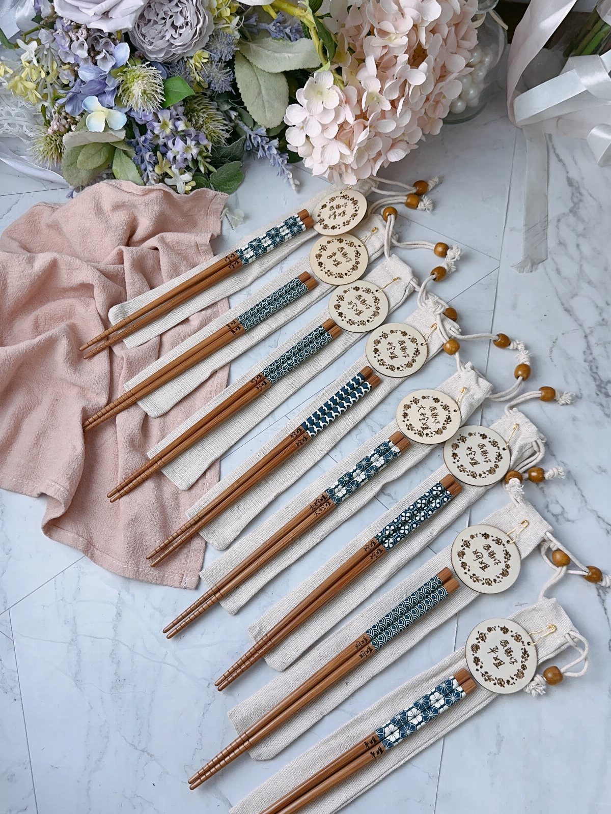 Engraved wooden chopsticks with blue patterns resting on white fabric pouches next to flowers.