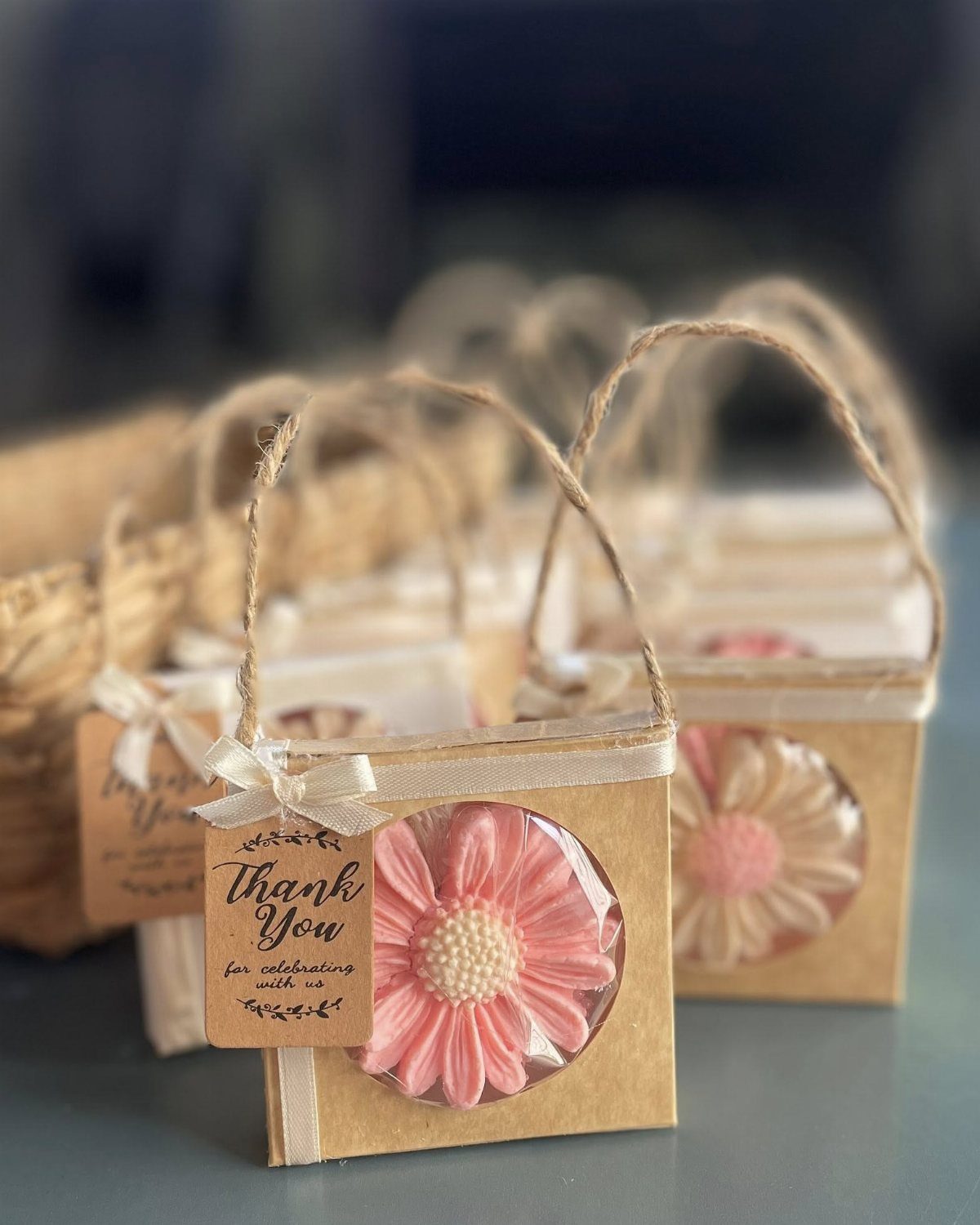 Flower-shaped pink and white handmade soap bars inside small cardboard gift boxes with twine handles.