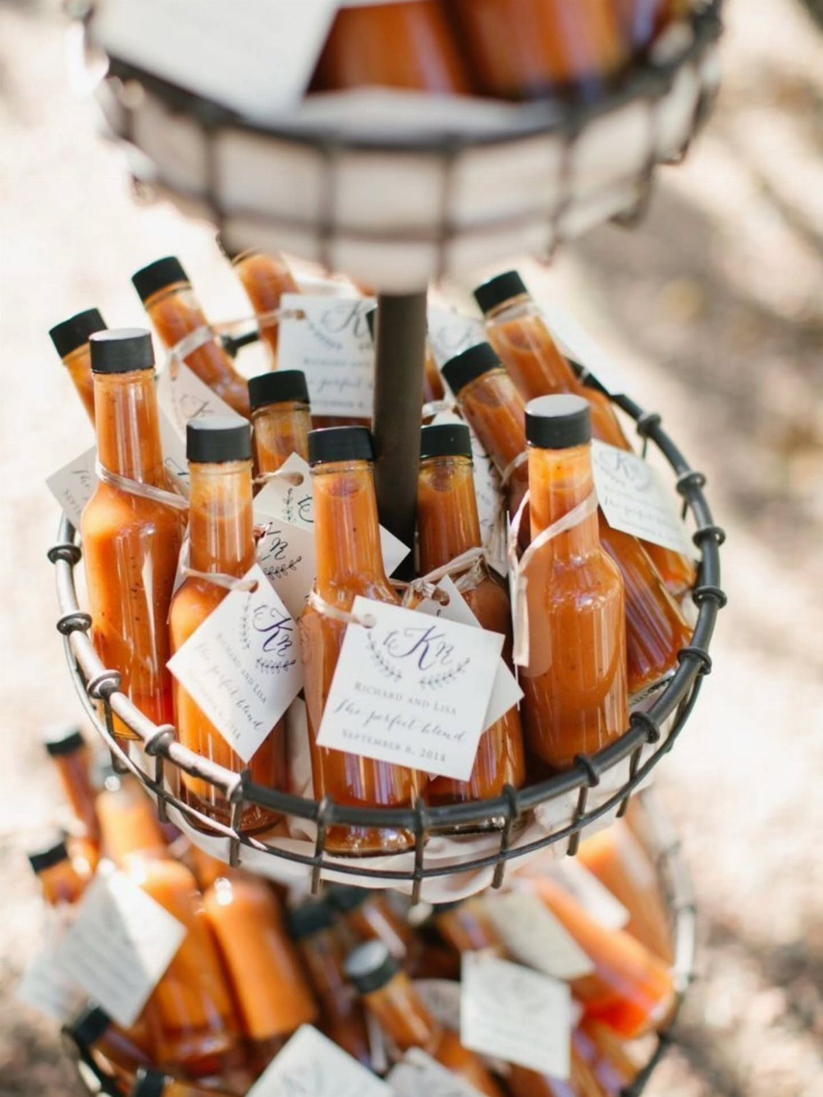Small glass bottles of orange hot sauce arranged in a tiered metal wire basket.