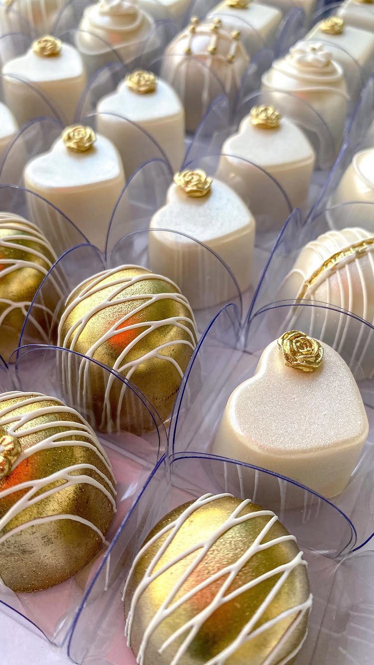 Assorted gold and white luxury chocolate truffles decorated with roses and intricate patterns in clear wrappers.