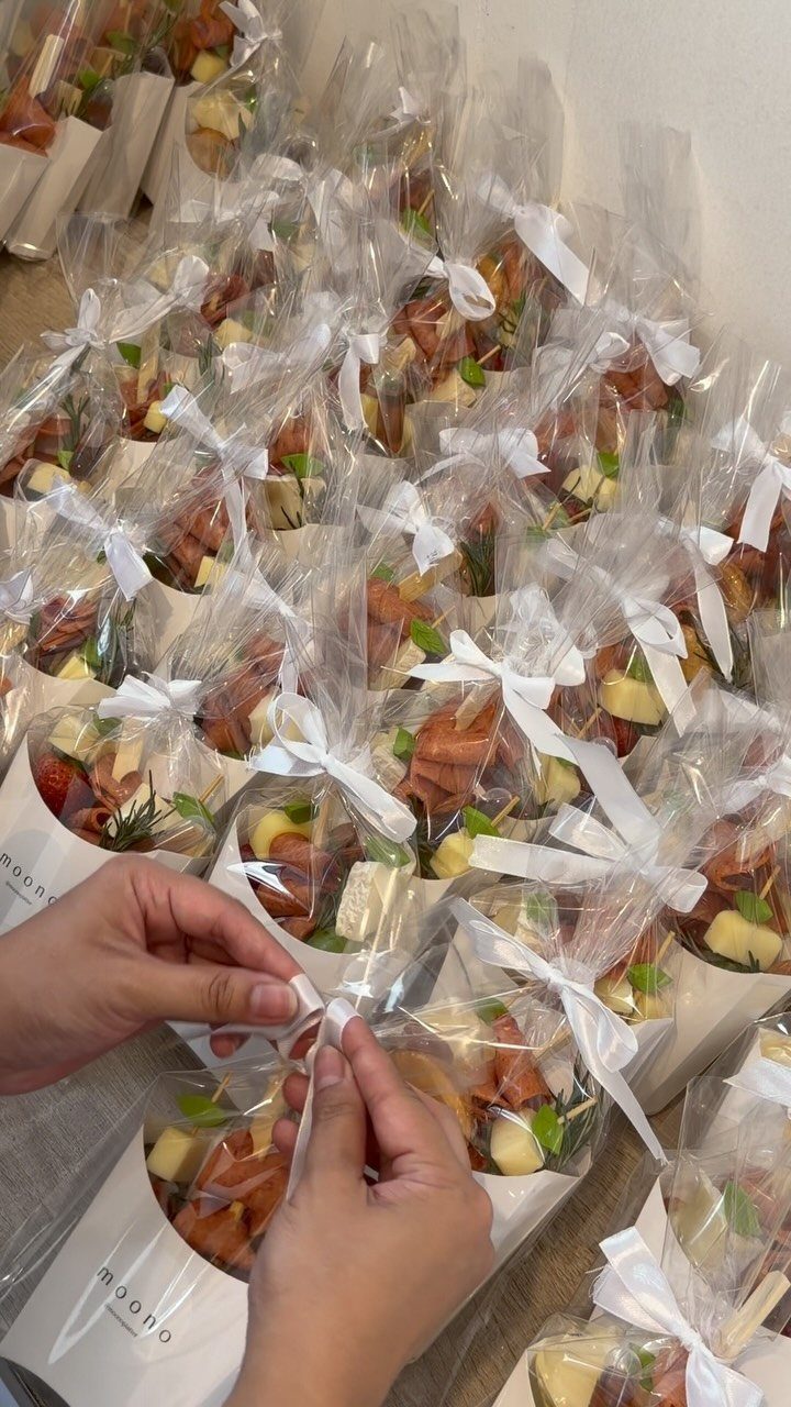 Hands tying a white ribbon onto a clear cellophane bag filled with small appetizers.