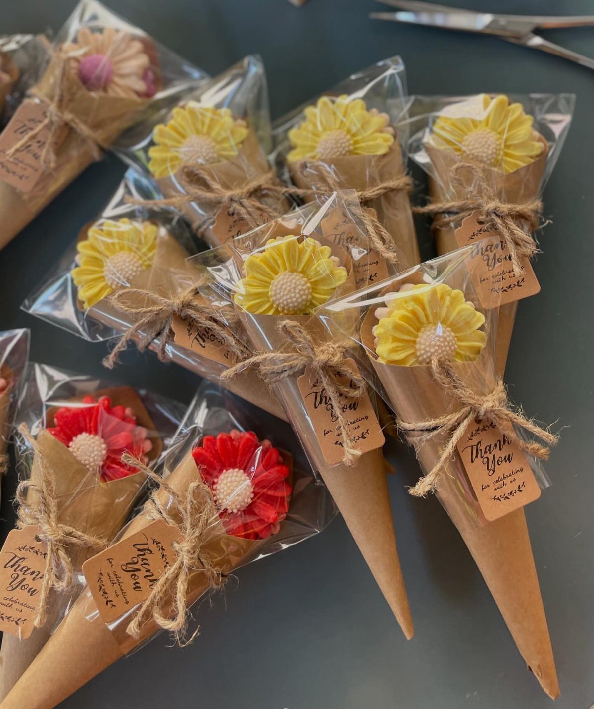 Small paper cones filled with colorful flowers, wrapped in plastic and tied with twine and thank you tags.