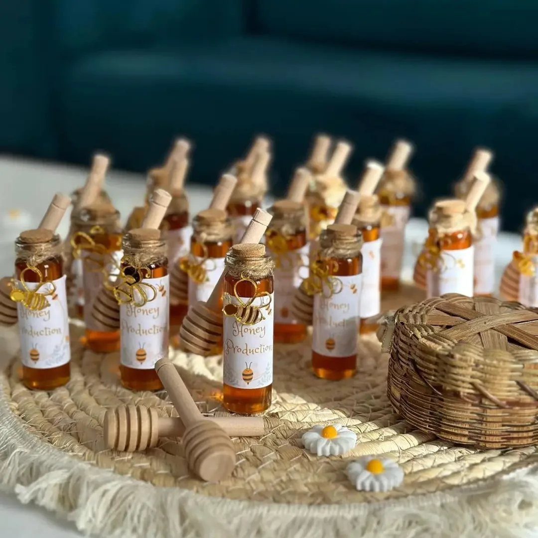 Small glass jars of honey with wooden dippers and bee decorations on a woven mat.